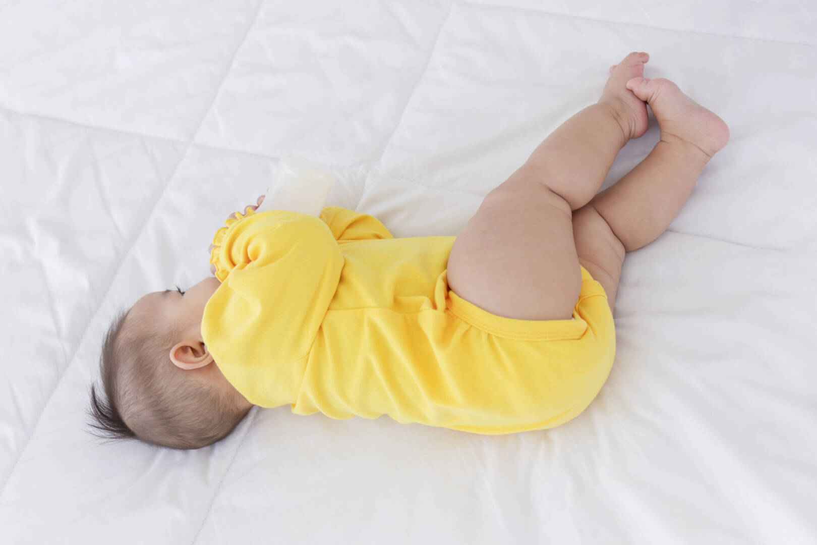 An Asian baby is sleeping on the bed and sucking the bottled mil