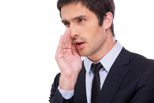 Businessman gossiping. Handsome young businessman telling gossips while holding hand near mouth and standing isolated on white background